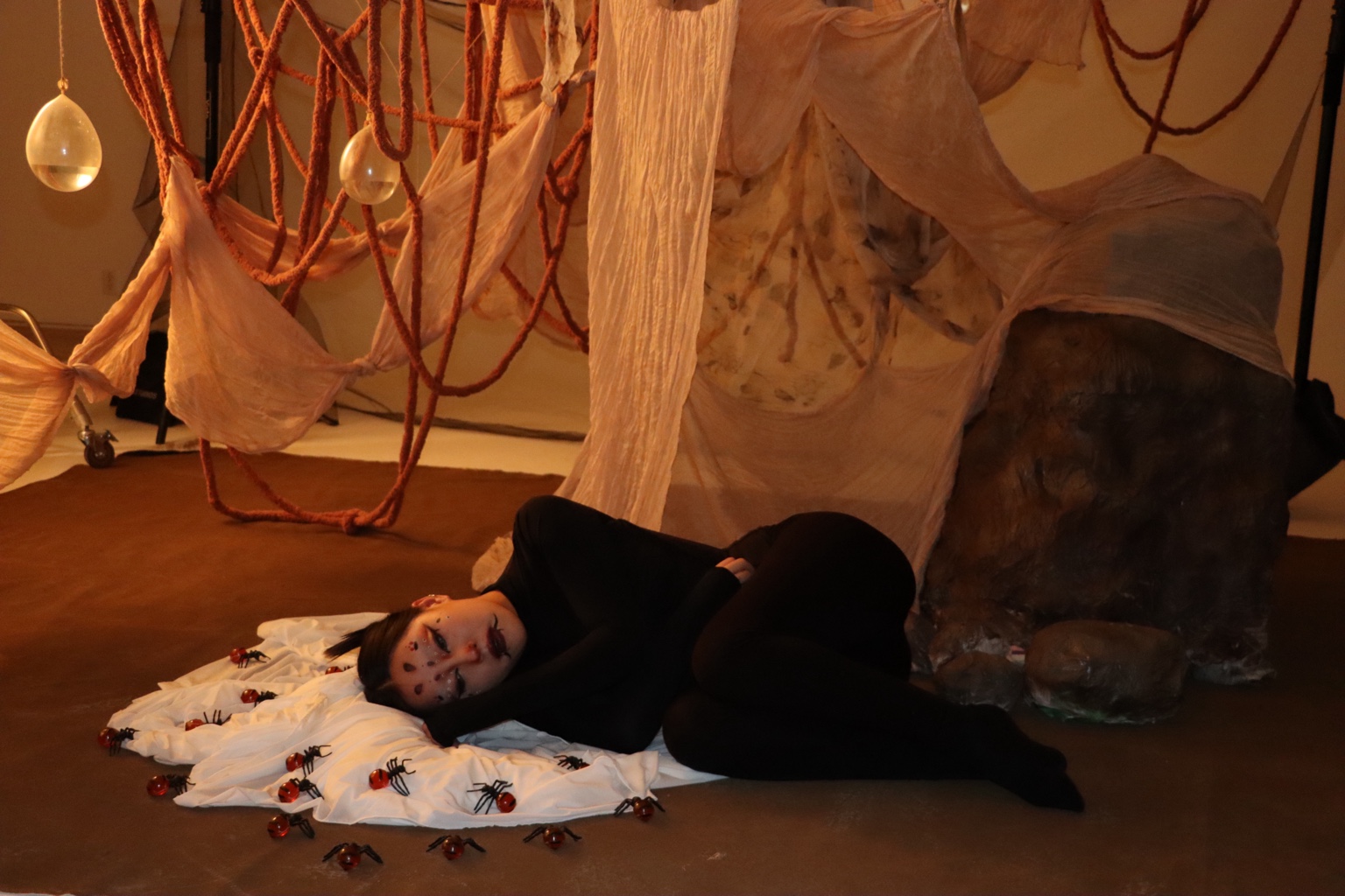 Wide view of the model and the set with draped fabric, suspended forms and insect props