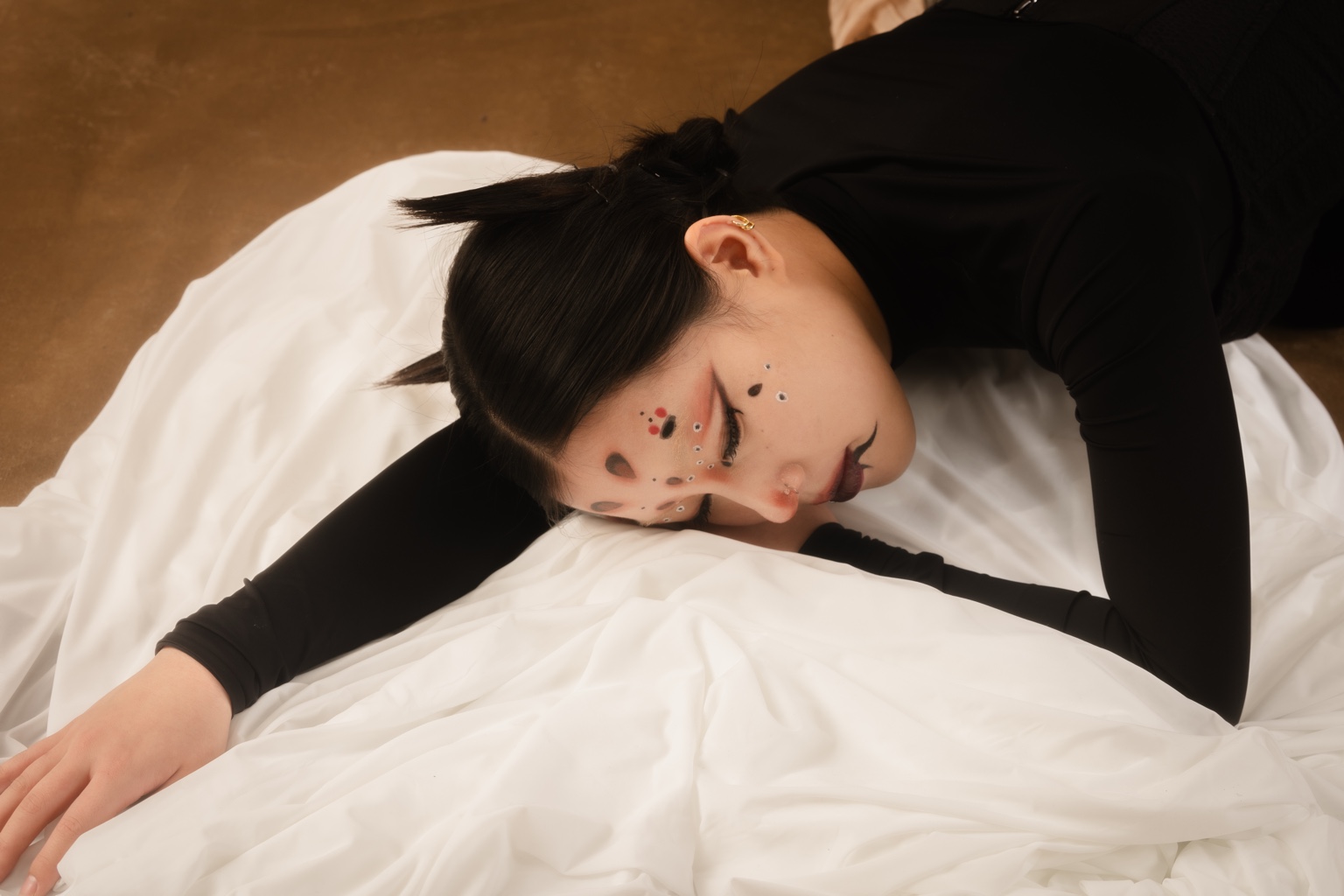 Model reclining on white fabric with graphic makeup